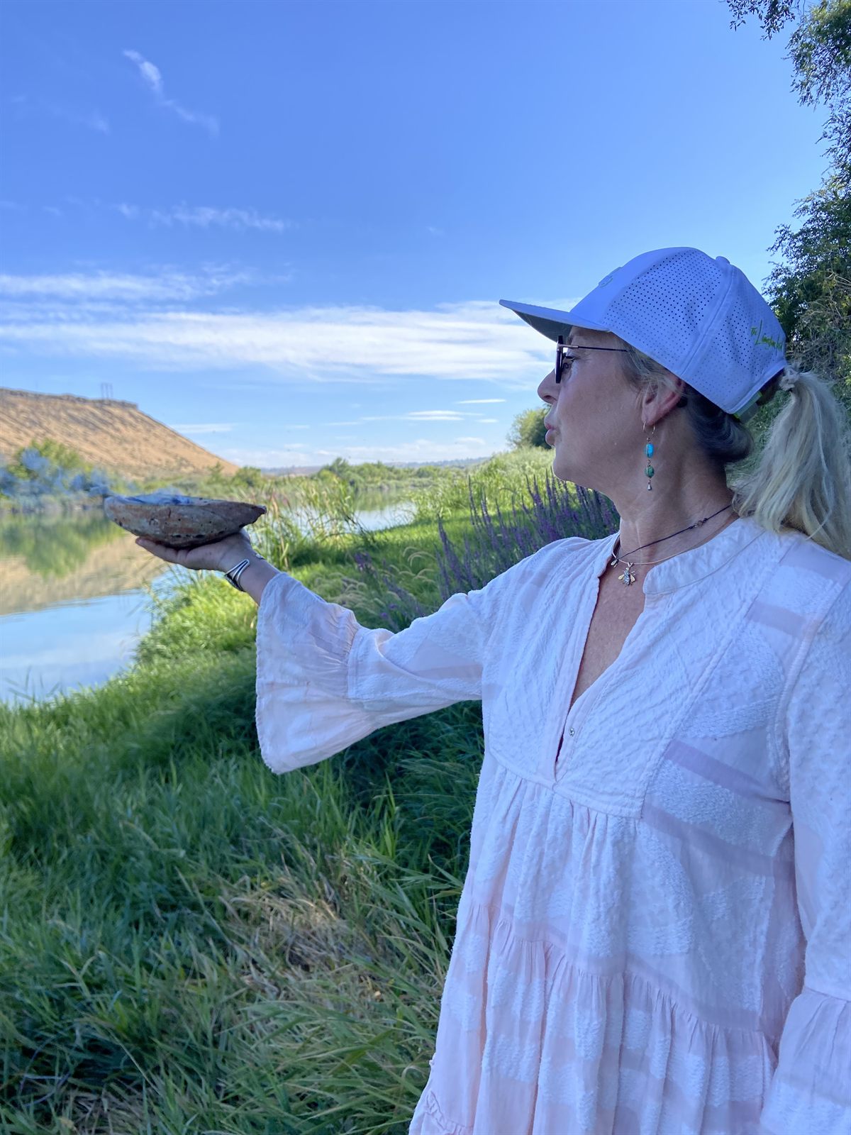 Tammara standing in tall grass at White Buffalo Crossing, holding a stone from the land